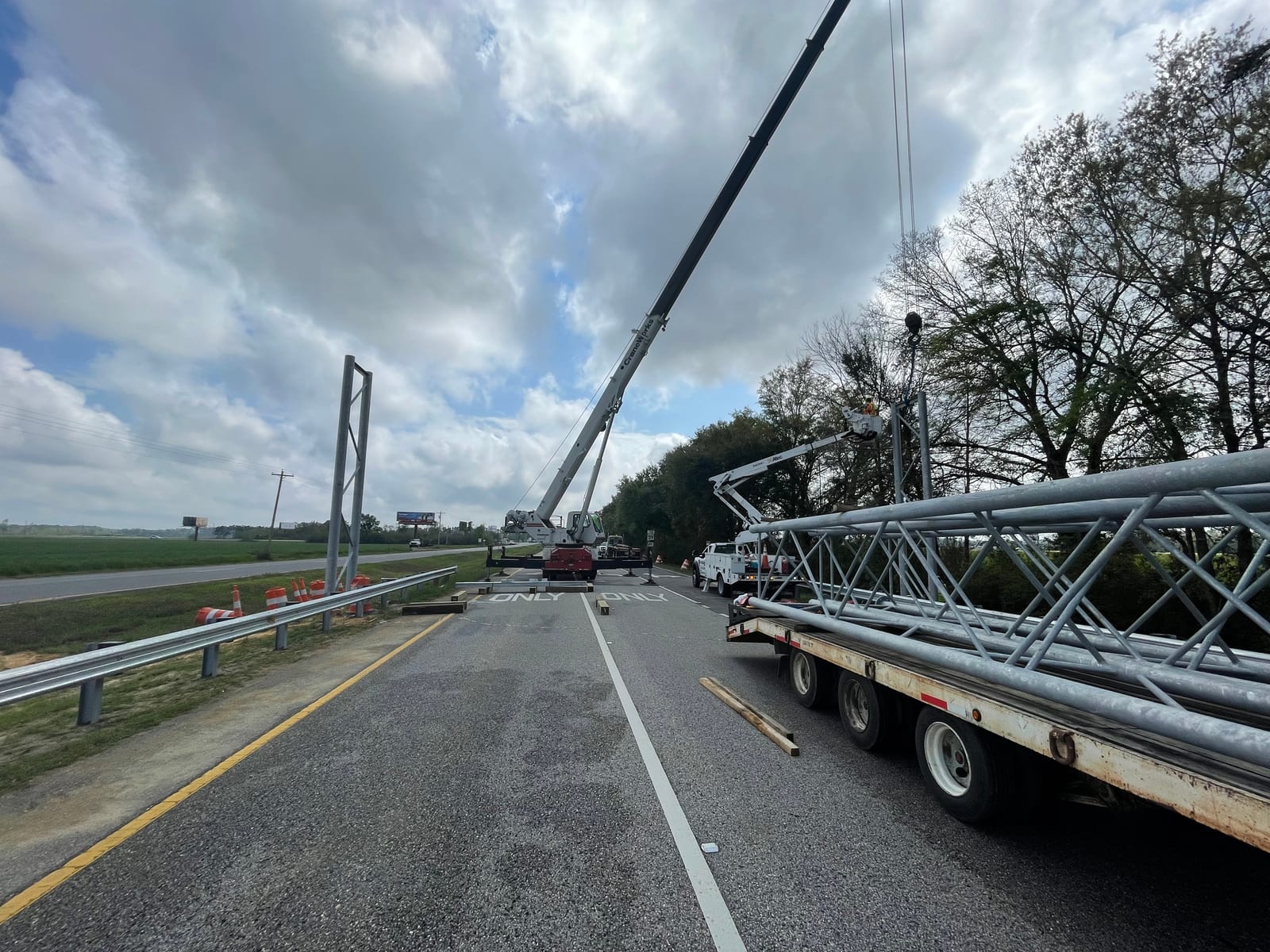 Full-span sign truss staged beside the roadway for crane installation